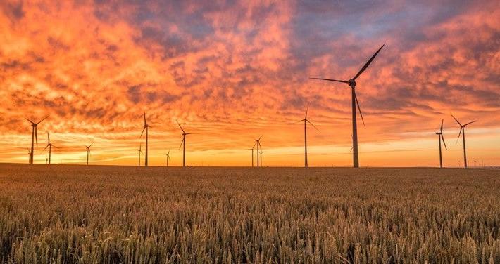 Wind turbines in a flat field against a vibrant sunset